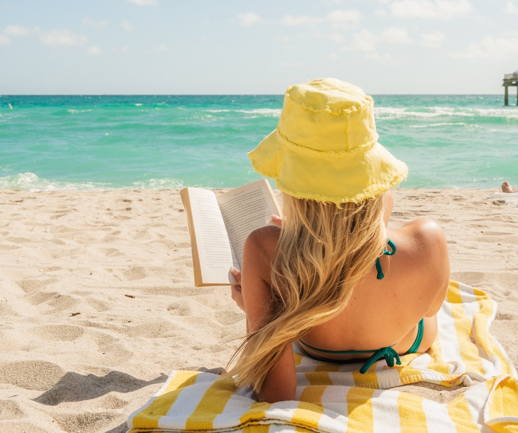 Woman reading a book laying down on sand in Miami beach