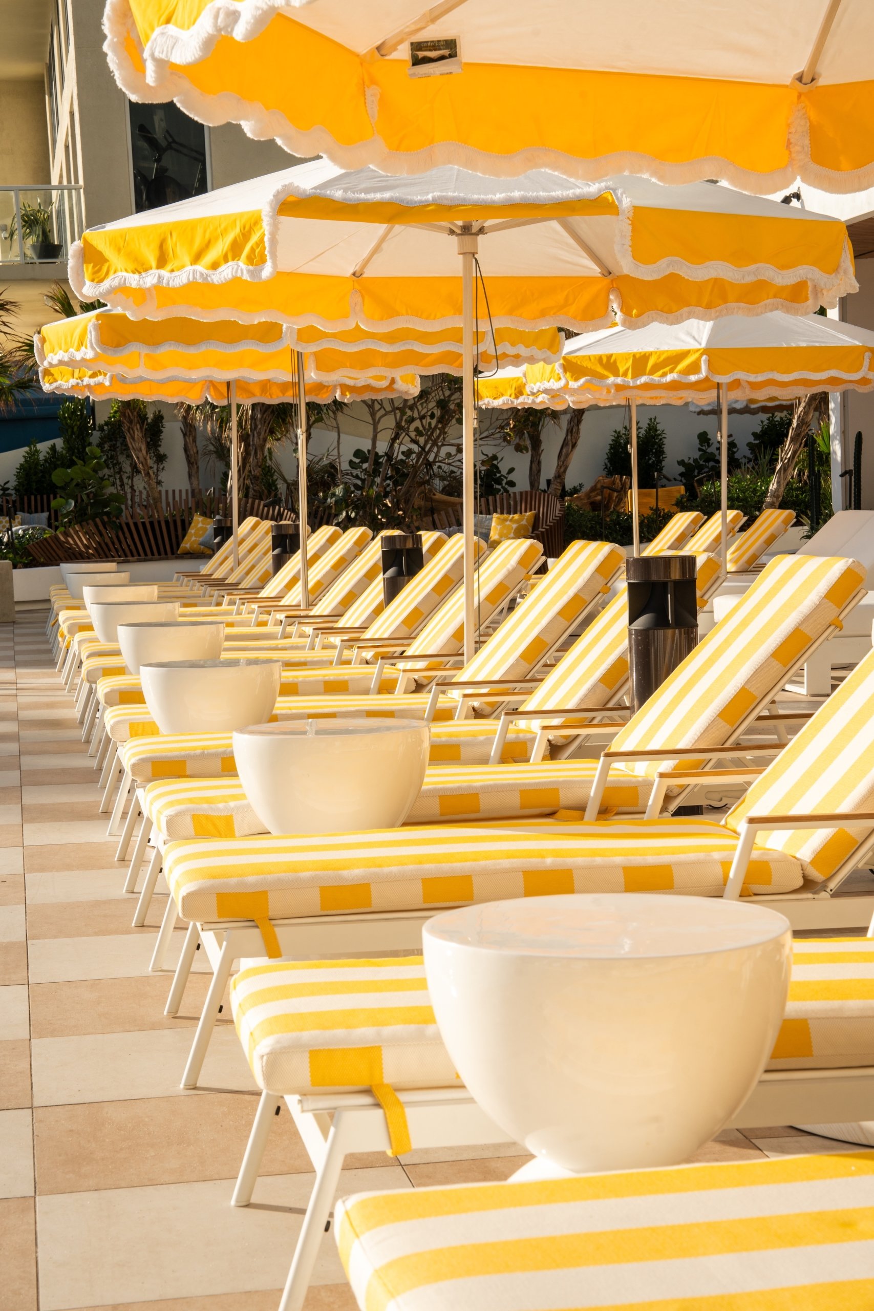 White round tables, and beach chairs under yellow parasols around swimming pool area