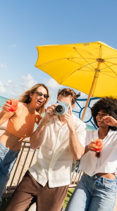 Three people with smiles under a yellow parasol at Newport Fishing Pier
