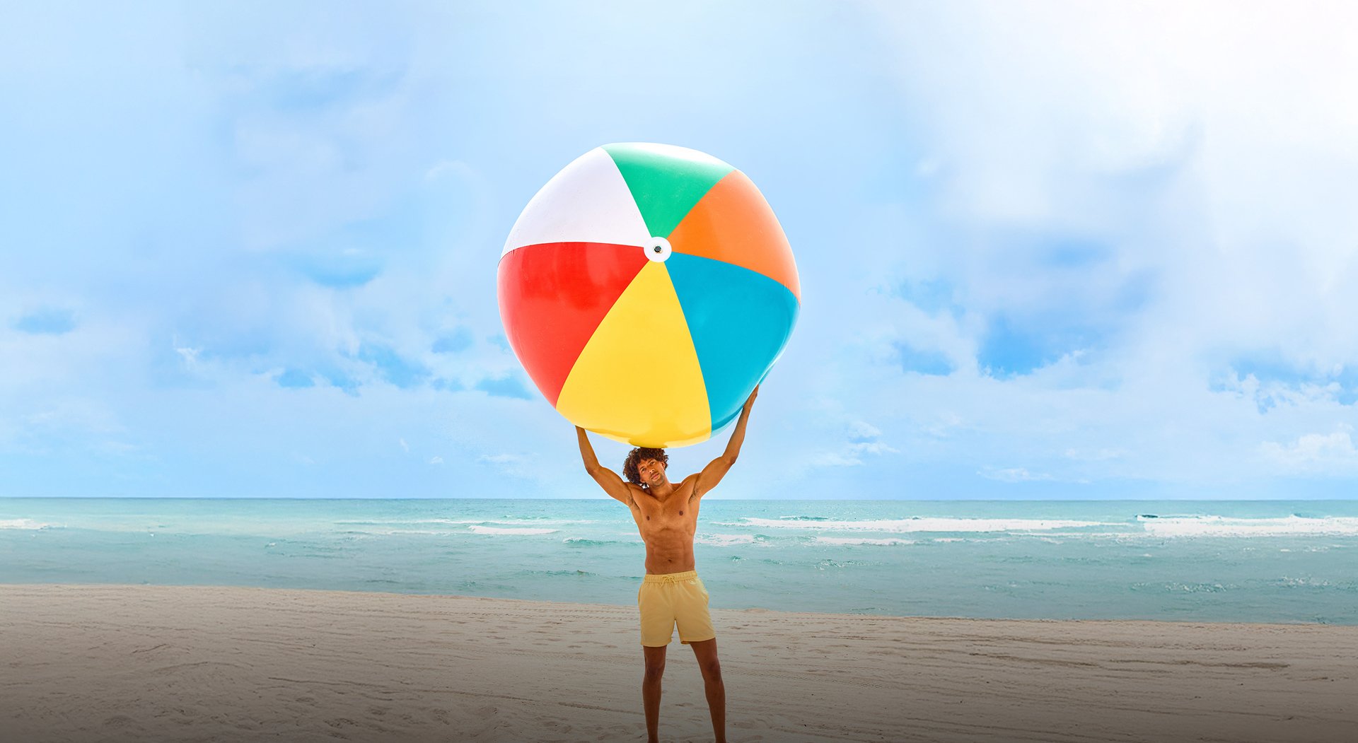 A man holding a huge colourful ball in the beach