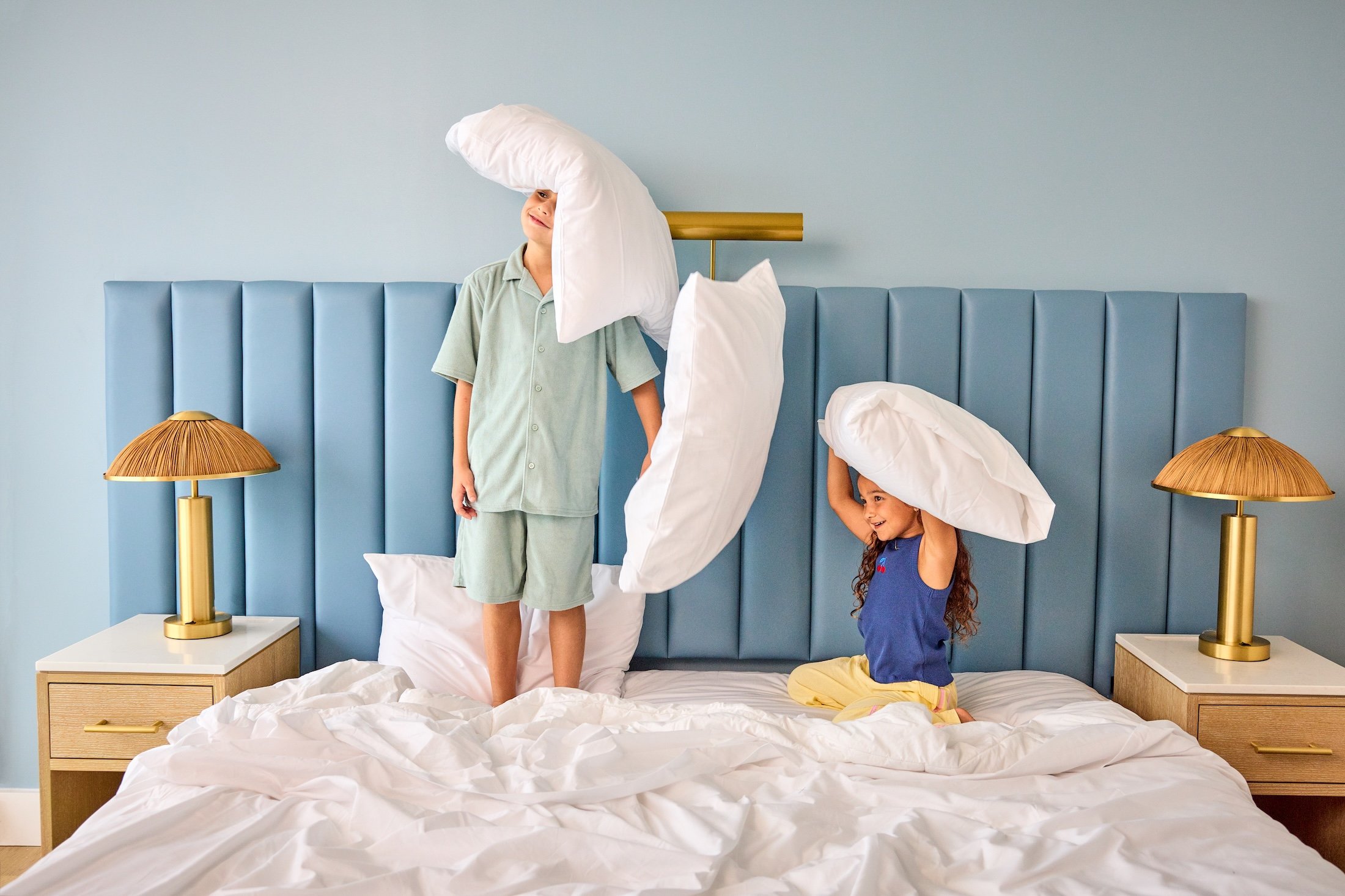 Two kids playing with pillows on a large bed at The Sunny Rooms