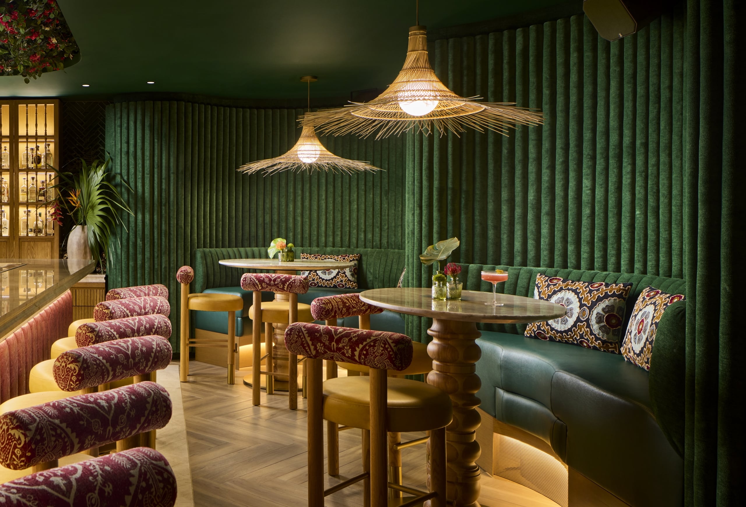 Cozy emerald green lounge with velvet banquettes, marble tables, and rattan pendant lighting at Julene.