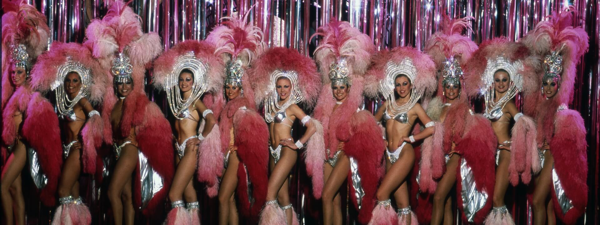Women lined up in pink showgirl outfits and headdresses